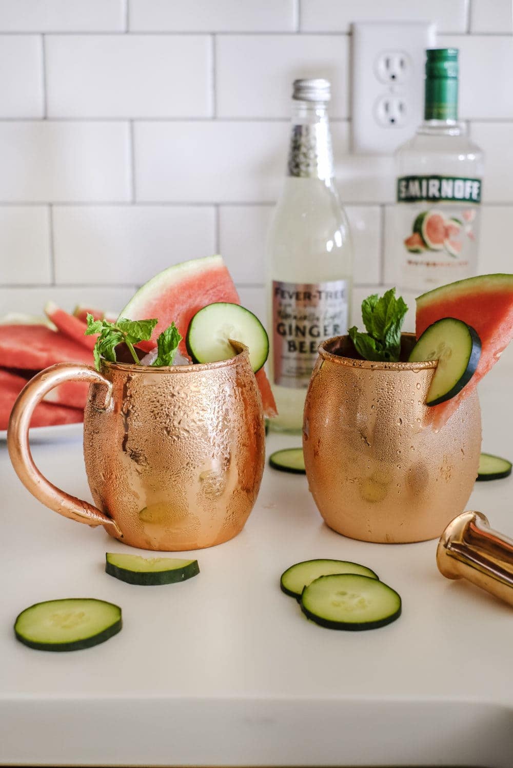 Two copper mugs with ingredients to make cucumber watermelon moscow mules