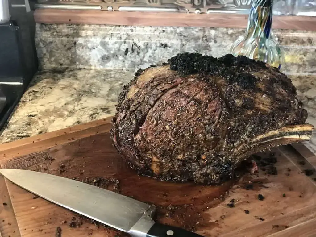 Roasted prime rib with knife on cutting board.