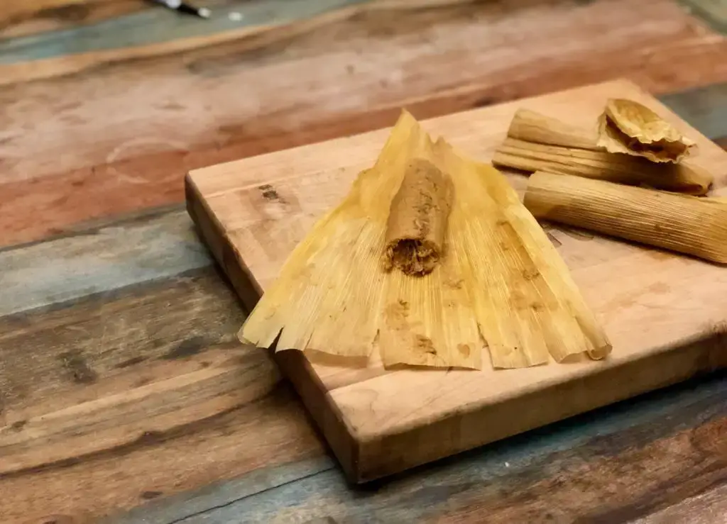 Corn husk tamales on a cutting board.