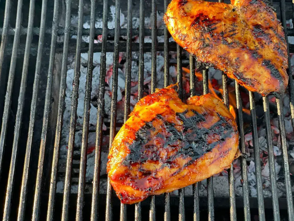 Two grilled chicken breasts on a grill.