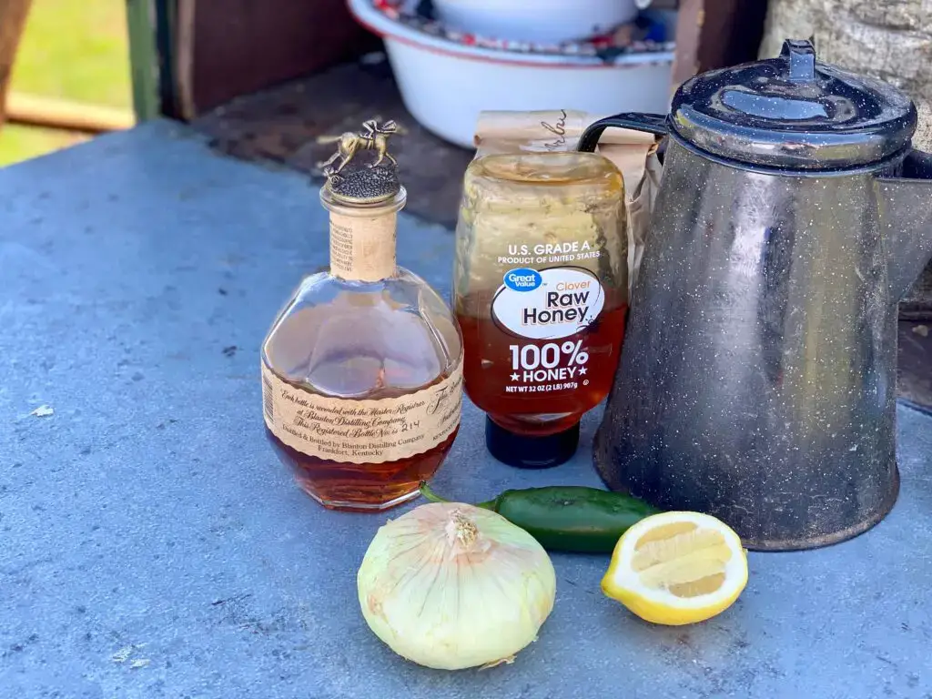 Whiskey, honey, lemon, and onion on table.