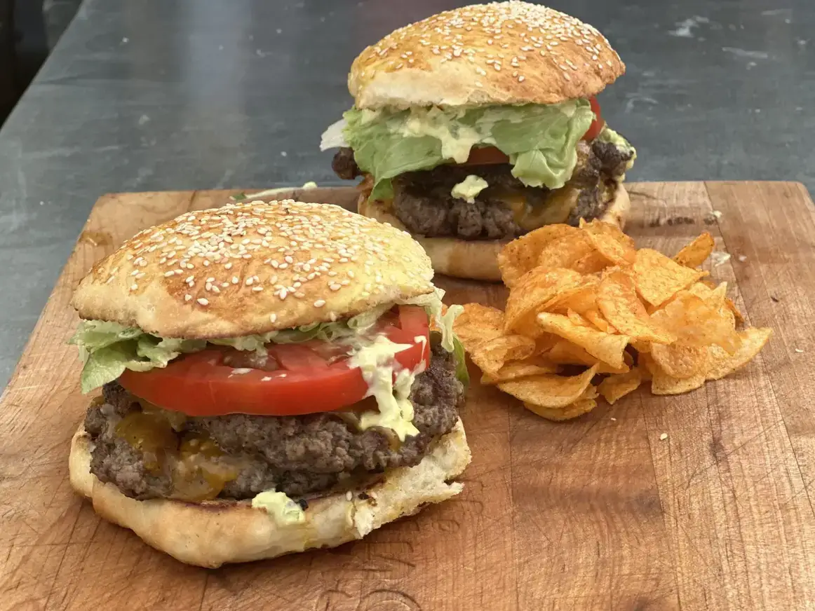 IMG_5820-2048x1536 (1) Two cheeseburgers with lettuce and tomato on a wooden board.
