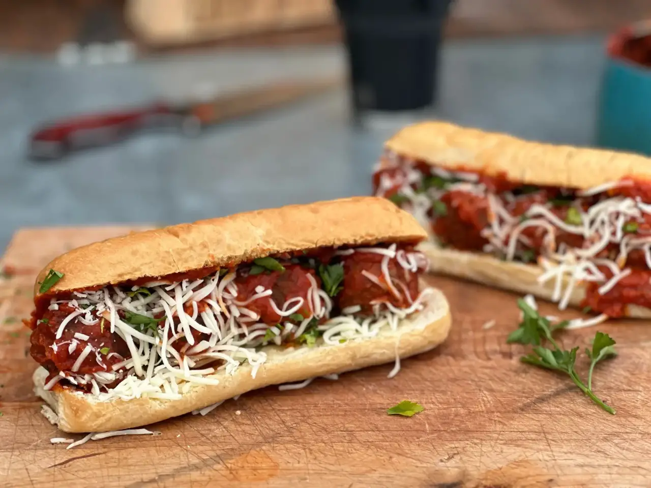 A meatball sandwich with cheese and herbs on top.